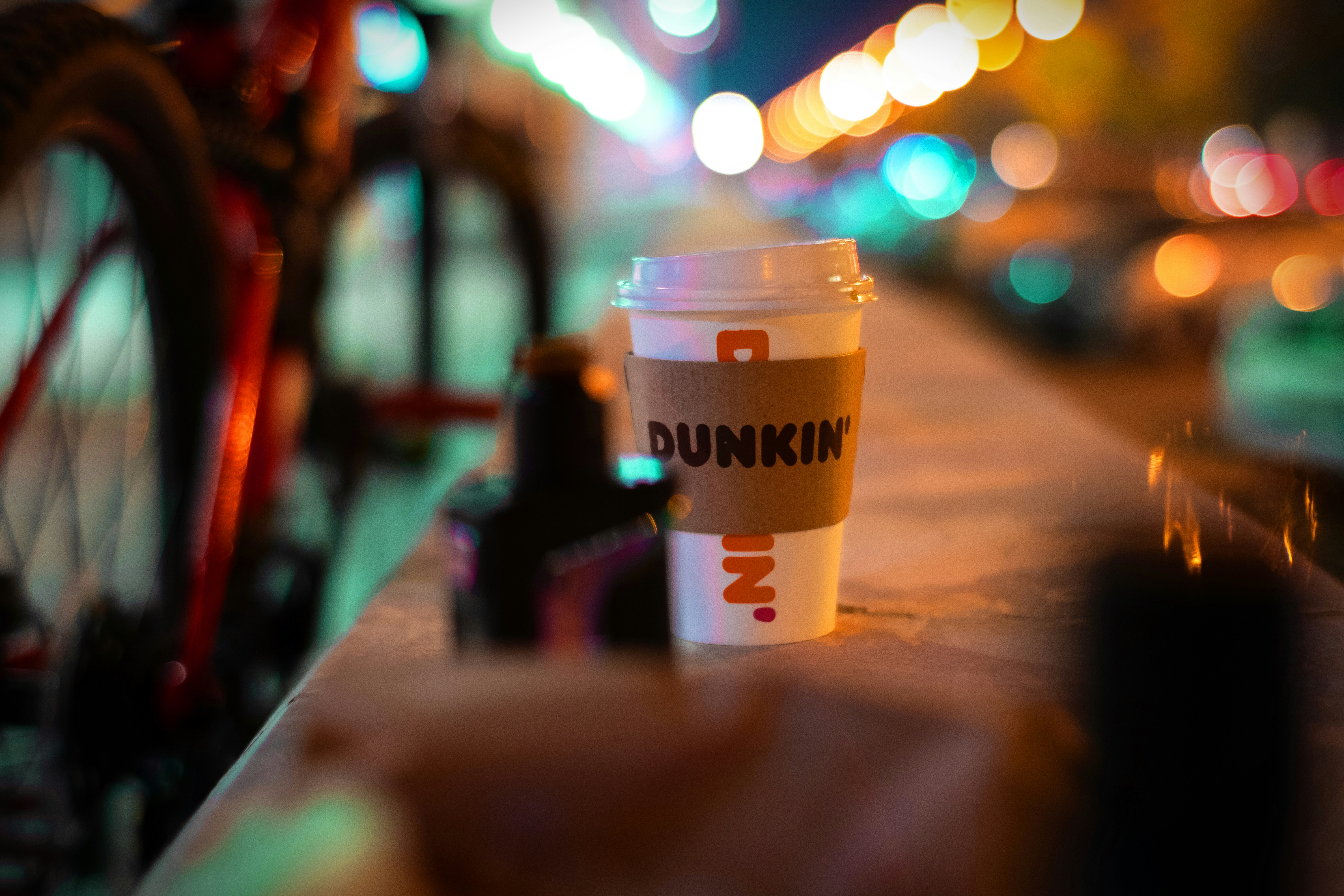 A smartphone displaying a Dunkin’ promotional offer for a free drink next to a coffee cup on a table, with a blurred business storefront in the background.
