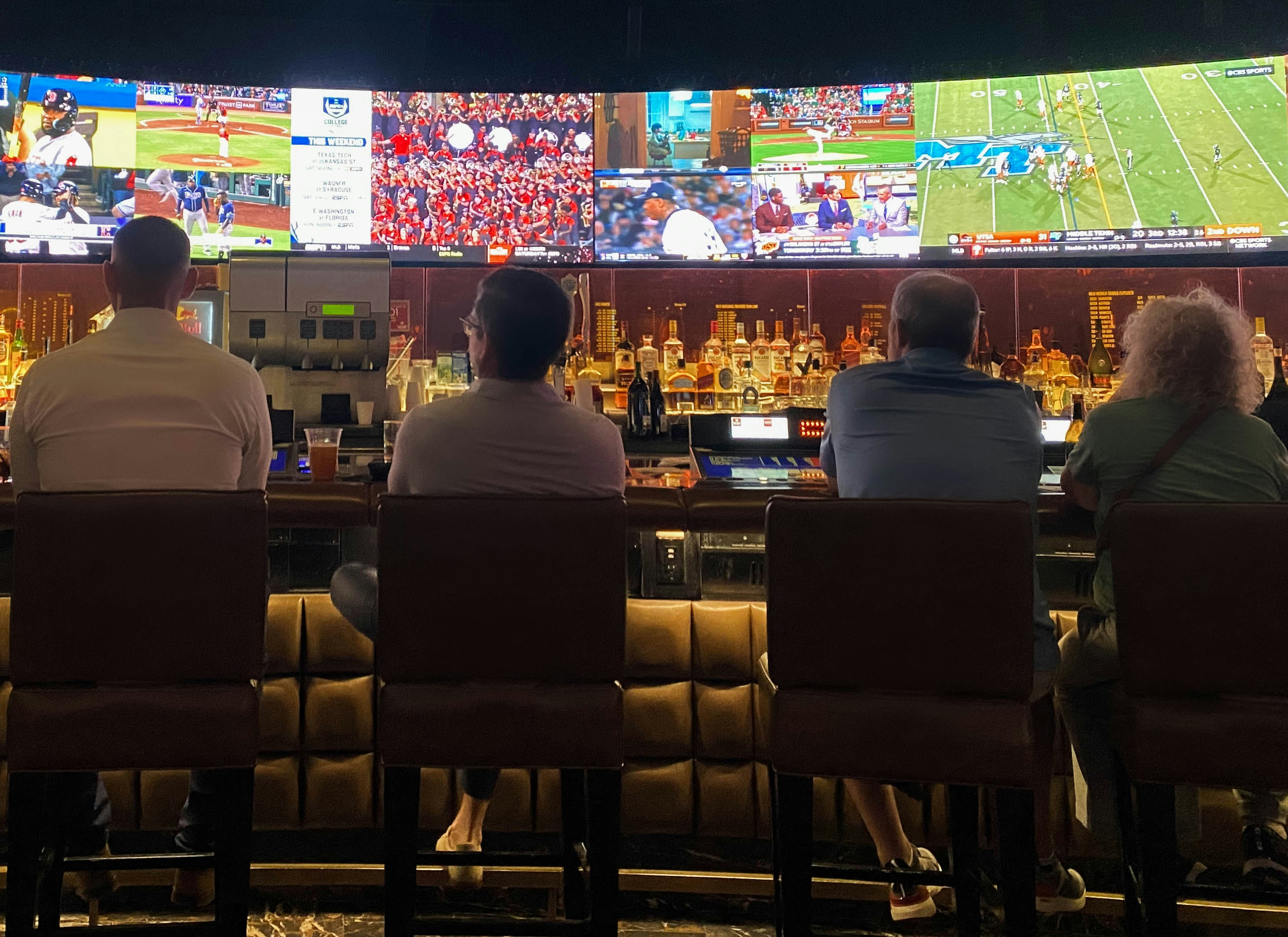 A crowded sports bar with patrons watching a baseball game on multiple large screens, with a smartphone displaying an automated text message response overlaid in the foreground.