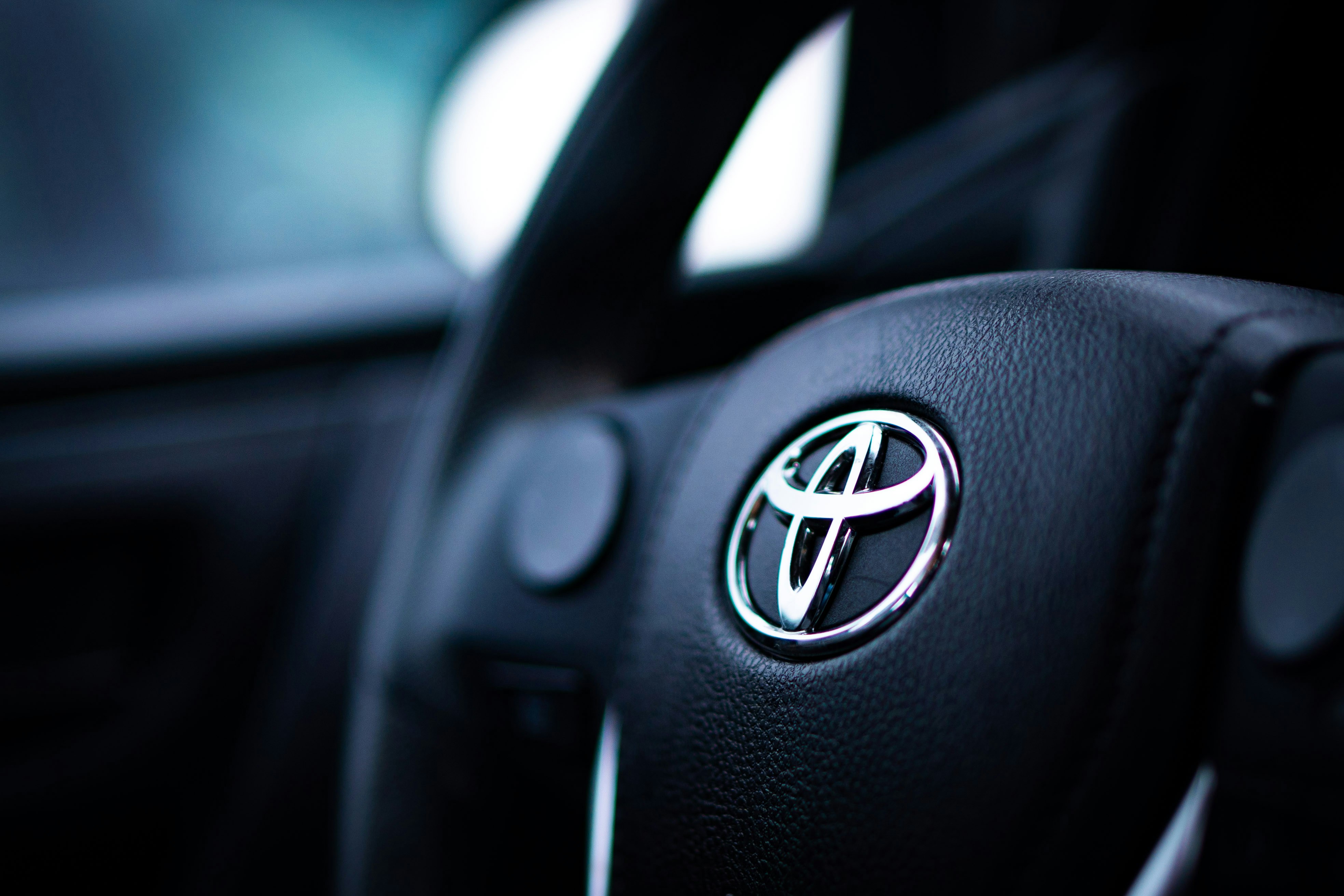 A Toyota Camry dashboard display showing a warning light, with a service advisor holding a tablet in the background